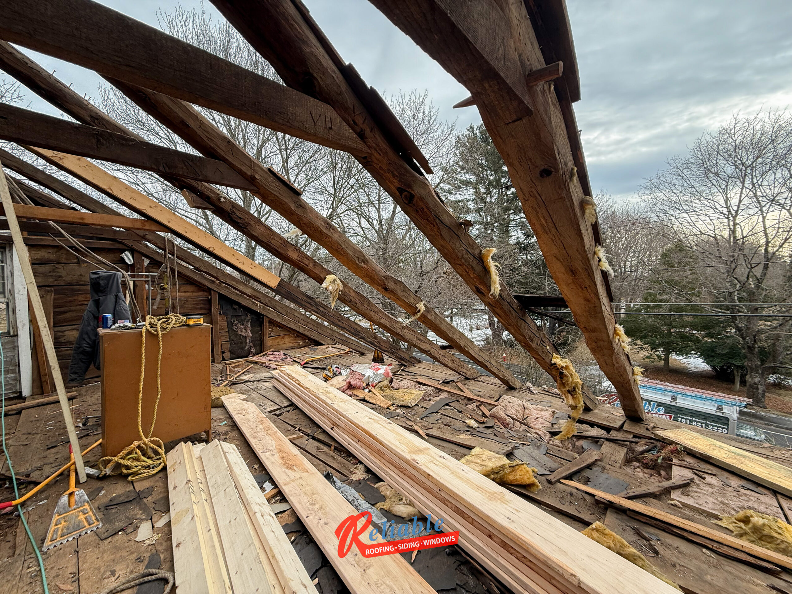 Roofing crew revealing hand-hewn rafters and Roman numeral carpenter marks in Raynham, Massachusetts.
